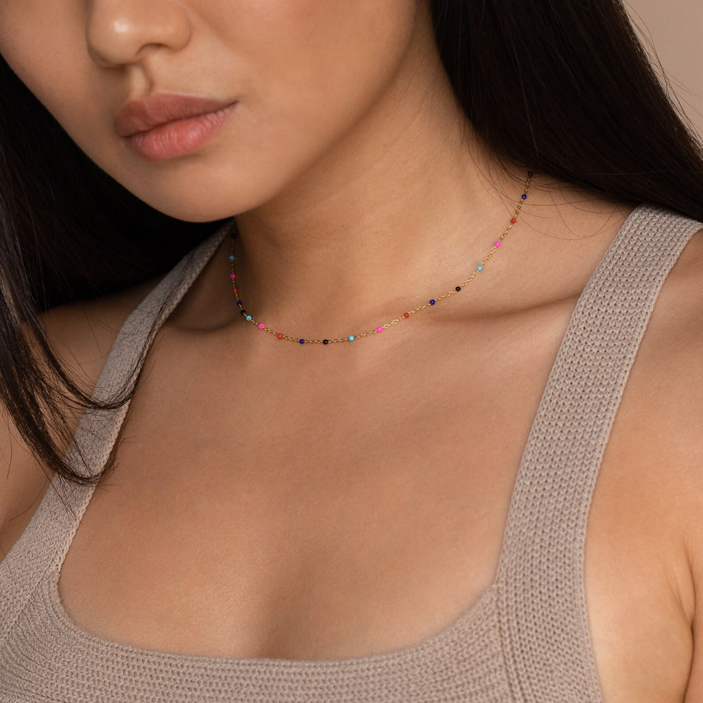 Woman wearing a beige textured tank top and the Rainbow Station Necklace, a delicate, colorful bead accessory.