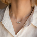 Woman wearing a cream blouse and the Peas in a Pod Necklace, featuring three pearls nestled in a silver pod pendant.