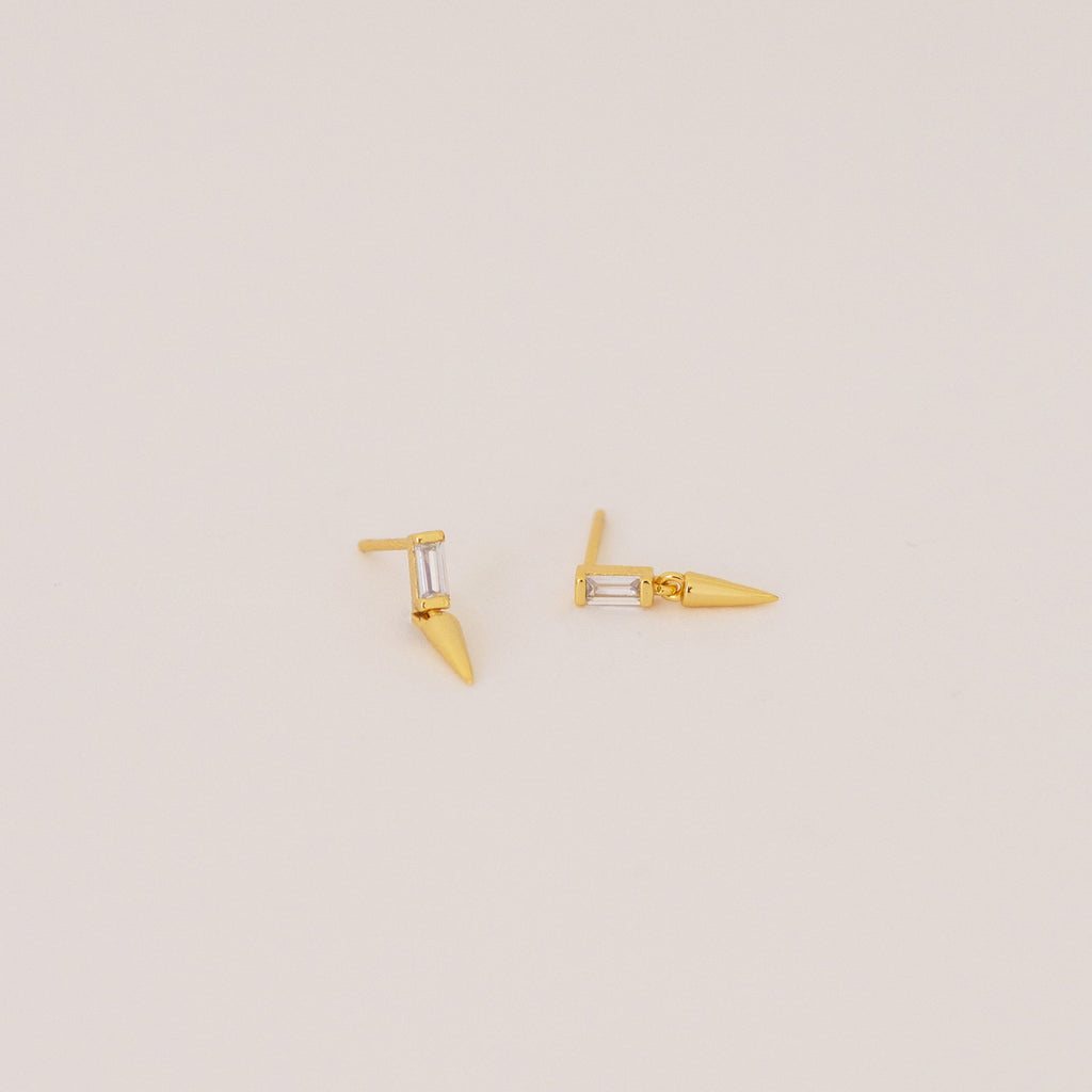The Wren Spike Studs are lightweight, small spike-shaped earrings featuring CZ baguette diamonds and a pointed spike detail, set against a plain background.