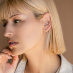 A woman with short blonde hair wears Astra Moon & Star Huggies, gazing thoughtfully to the side.