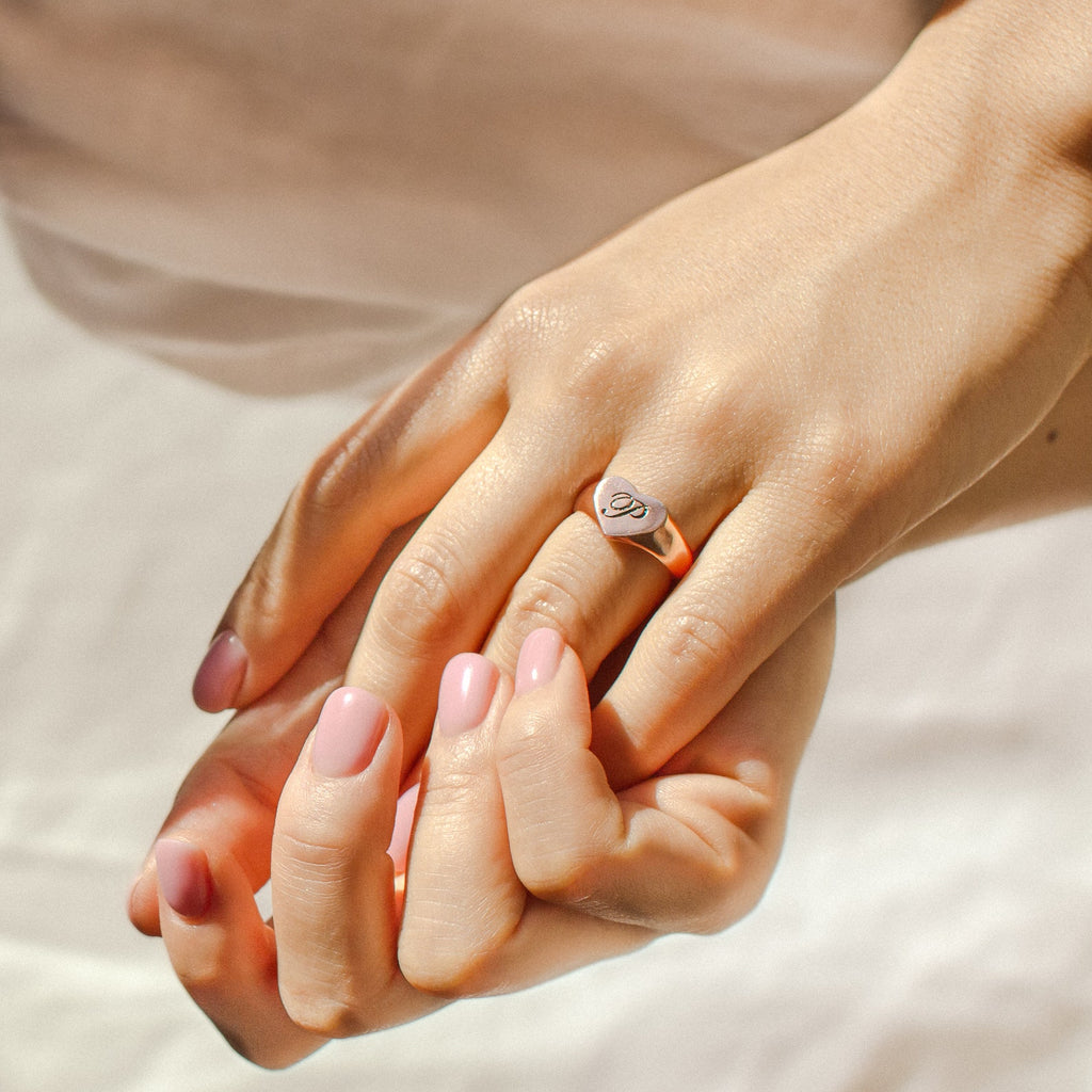 A hand with light pink nails wears a silver Traditional Initial Heart Signet Ring engraved with the letter “D” on the ring finger—an ideal personalized or anniversary gift.