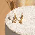 Pave Initial Huggies, featuring gold hoops with Eiffel Tower-shaped crystal pendants, offer a charming style—ideal as a personalized gift or for mixing and matching earrings on any occasion. Shown on a textured white background.