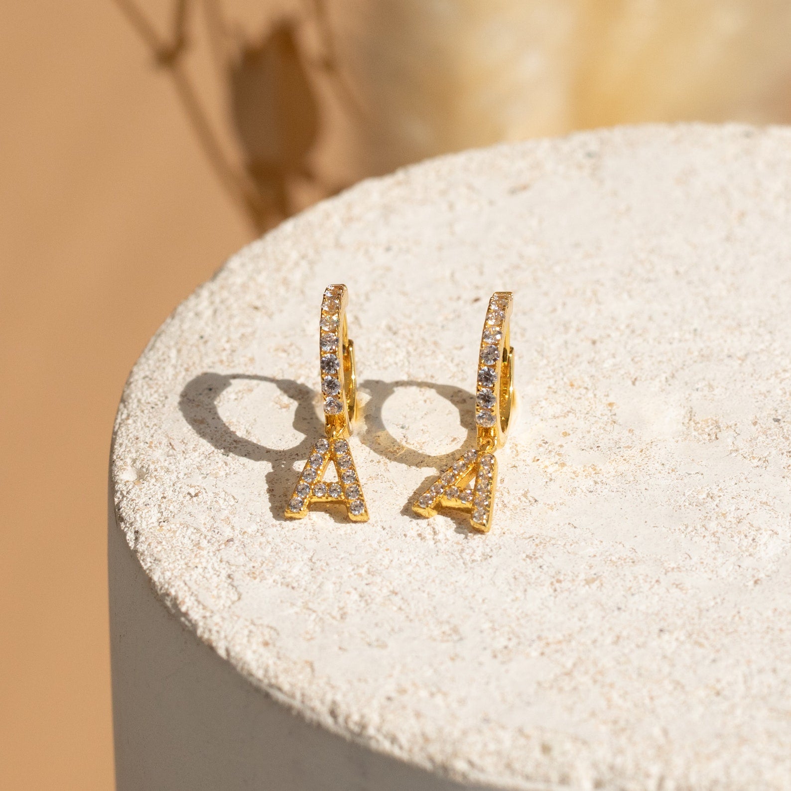 Pave Initial Huggies, featuring gold hoops with Eiffel Tower-shaped crystal pendants, offer a charming style—ideal as a personalized gift or for mixing and matching earrings on any occasion. Shown on a textured white background.
