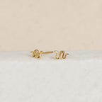 Dainty jewelry lovers will adore the Tiny Python Studs—petite gold earrings with elegant curves, perfect for a boho-luxe style and shown on a white textured background.