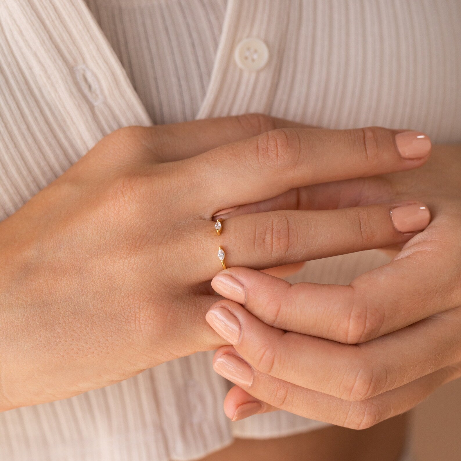 Close-up of a hand wearing the Celeste Duo Marquise Ring, showcasing its delicate open design with small gemstones, set against a cream-colored shirt.