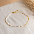 A gold chain and small white pearl bracelet rest on soft cream fabric with pampas grass, perfectly complementing the Pearl & Paperclip Chain Necklace for an elegant, coordinated look.