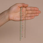 A hand displays Beaded Station Necklaces—delicate, trendy jewelry chains featuring vibrant beads—set against a neutral beige background.