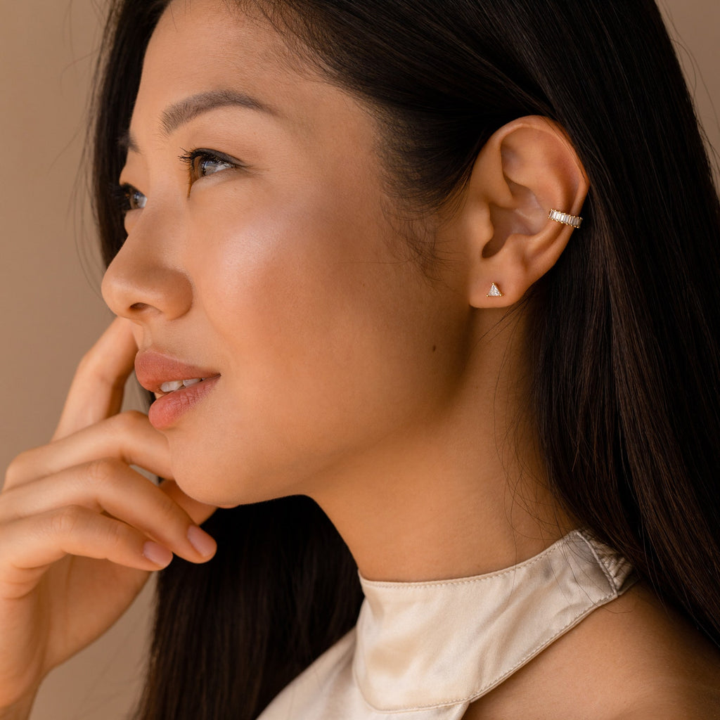 Woman with long dark hair, wearing a satin top and modern classic jewelry—minimal gold Trixie Diamond Studs accented with triangle-shaped diamonds—gazes thoughtfully to the side.