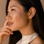 Woman with long dark hair, wearing a satin top and modern classic jewelry—minimal gold Trixie Diamond Studs accented with triangle-shaped diamonds—gazes thoughtfully to the side.
