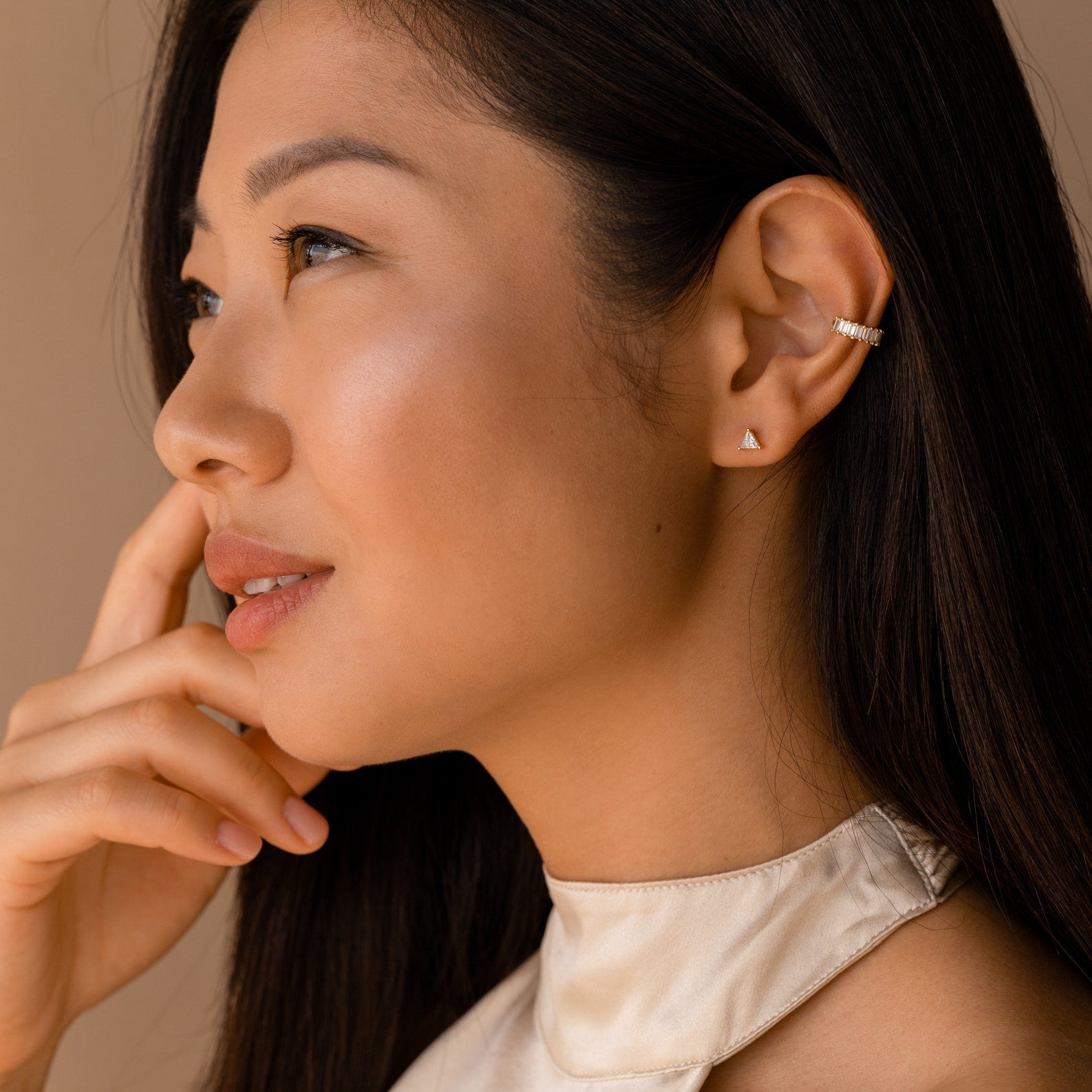 Woman with long dark hair, wearing a satin top and modern classic jewelry—minimal gold Trixie Diamond Studs accented with triangle-shaped diamonds—gazes thoughtfully to the side.