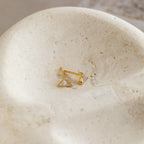 The Trixie Diamond Studs—gold, triangle-shaped earrings—rest on a textured, off-white stone surface, exemplifying modern classic jewelry style.