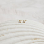 The Trixie Diamond Studs, gold triangular earrings with clear stones, showcase modern classic style and are beautifully presented on a textured white seashell background.
