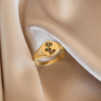 The Birth Flower Signet Ring features engraved floral designs and rests on soft, beige satin—perfect for anyone who treasures personalized jewelry.