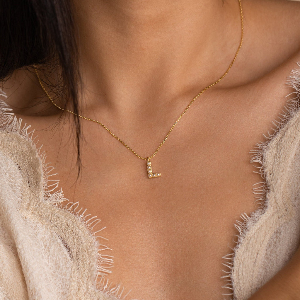 The Pearl Letter Necklace, featuring an L pendant and delicate pearls, adorns a woman's bare neck and upper chest.
