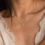 The Pearl Letter Necklace, featuring an L pendant and delicate pearls, adorns a woman's bare neck and upper chest.