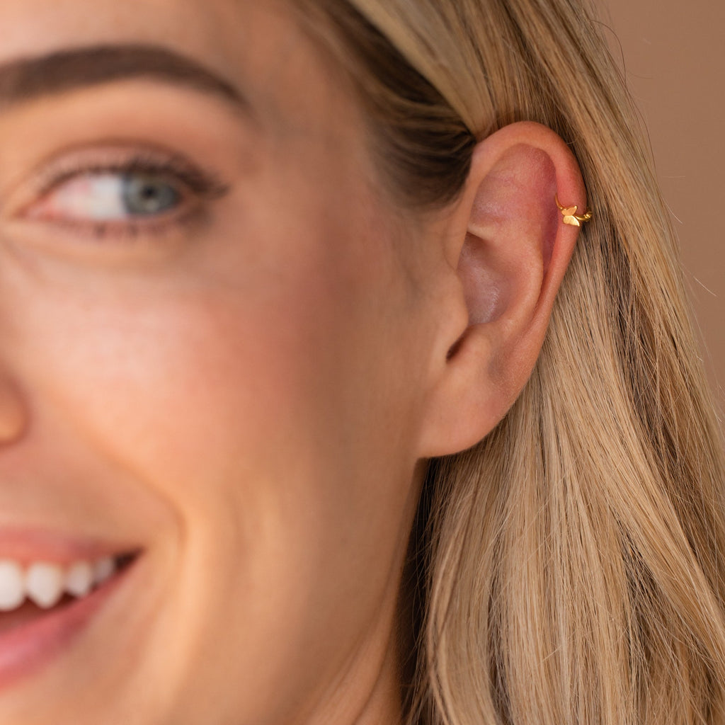 Smiling model with her hair tucked behind her ear, showcasing the butterfly huggie in a cartilage piercing.