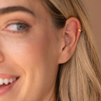 Smiling model with her hair tucked behind her ear, showcasing the butterfly huggie in a cartilage piercing.