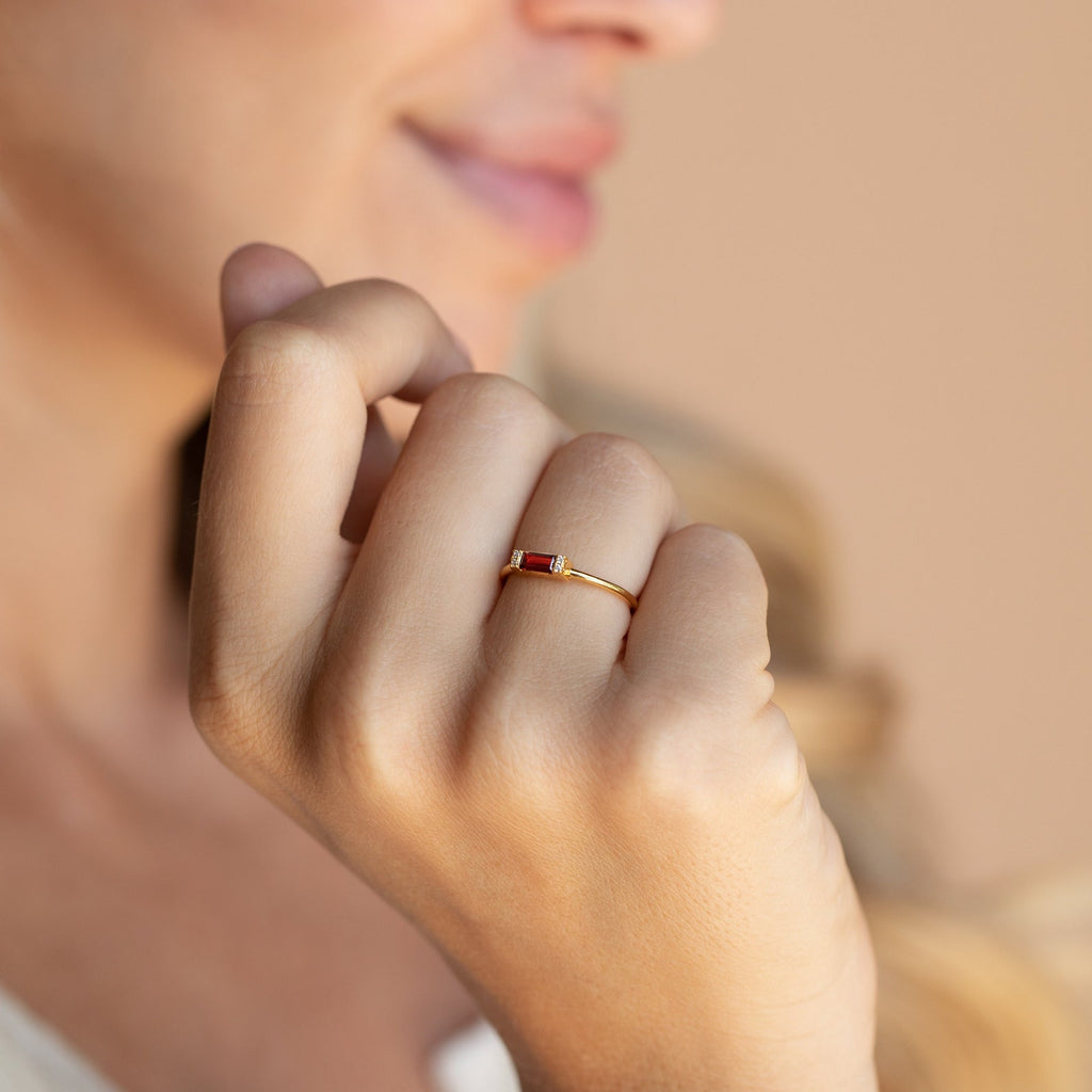 A woman’s hand with the Empire Garnet Ring—a thin gold band set with a small garnet—held near her face.
