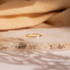 The Eloise Opal Ring, featuring a delicate gold band and a small iridescent opal gemstone, rests on a textured stone surface, embodying minimalist elegance.