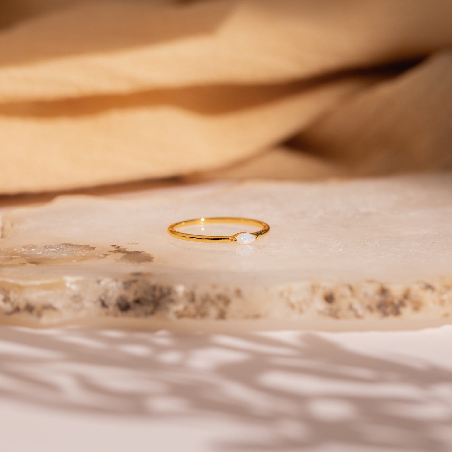 The Eloise Opal Ring, featuring a delicate gold band and a small iridescent opal gemstone, rests on a textured stone surface, embodying minimalist elegance.