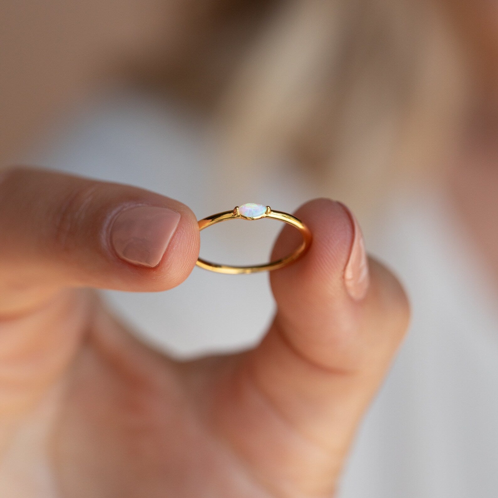A hand holds the Eloise Opal Ring, featuring a delicate gold band and a small, iridescent white opal—ideal for minimalism lovers.