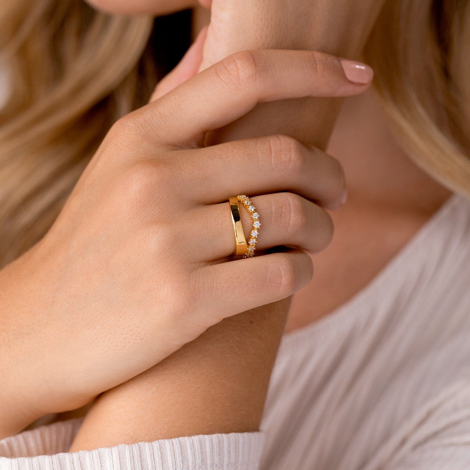 Close-up of a hand wearing two gold rings—a plain band and the Wave Diamond Duo Ring—ideal for stacking ring lovers, set against a light fabric background.