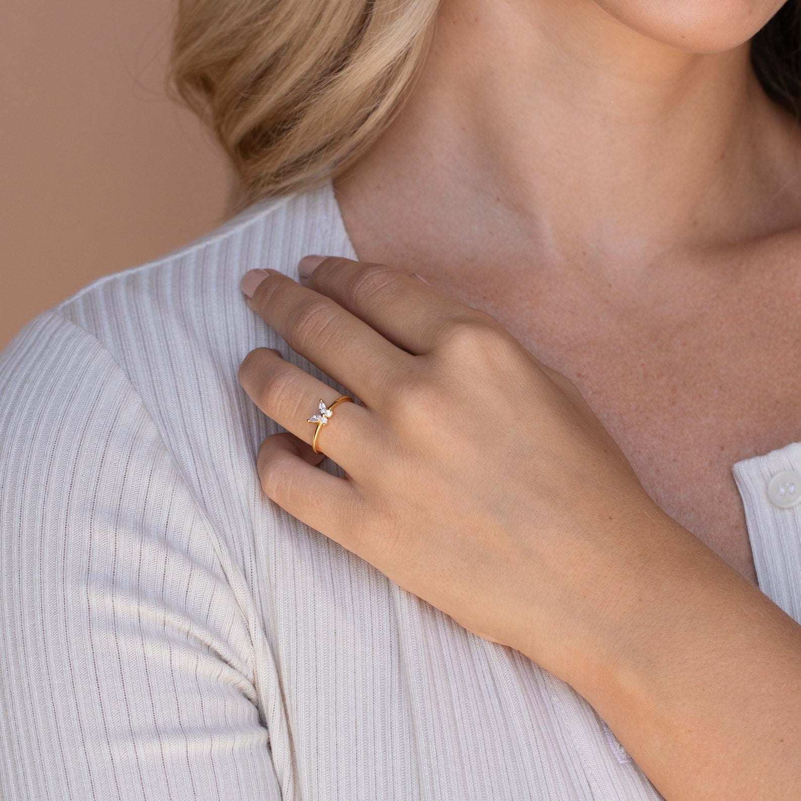 A woman rests her hand on her chest, showcasing the Mariposa Diamond Ring with a sparkling clear gemstone on her finger.