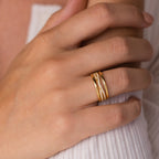 A hand wearing the Amani Pave Twist Ring, featuring embedded small diamonds, rests on light-colored fabric.
