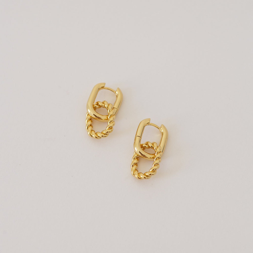 Kenzie Chain Link Earrings feature a twisted gold design for an edgy look, shown against a simple light background.