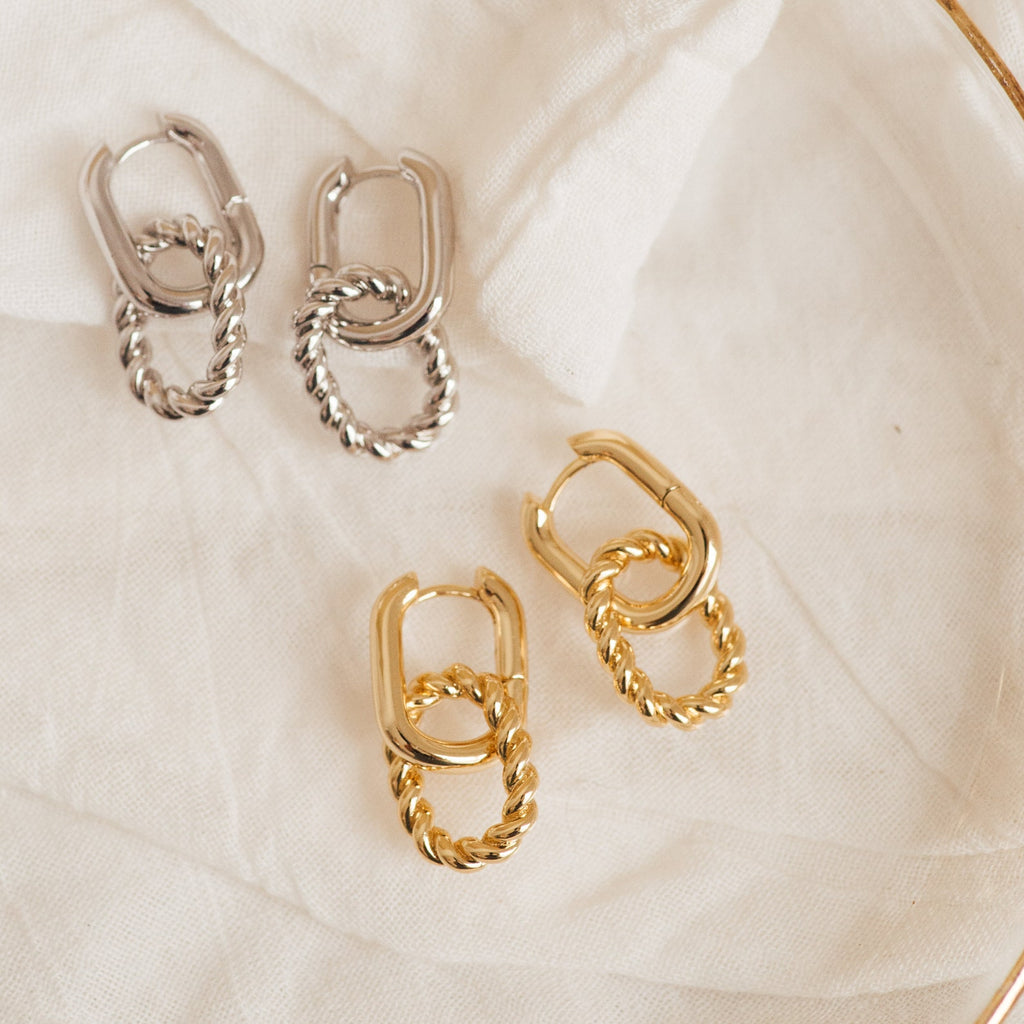 Two pairs of Kenzie Chain Link Earrings—one gold, one silver—make a bold statement against soft white fabric, perfect for those who love edgy jewelry.