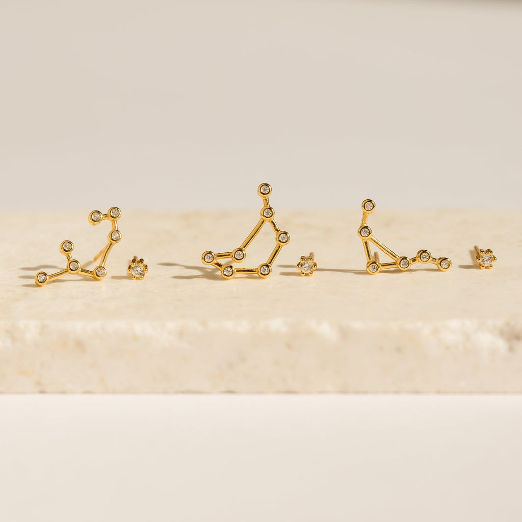 Five Constellation Earrings rest on a light stone surface, illuminated by soft lighting and inspired by astrology.