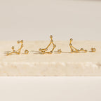 Five Constellation Earrings rest on a light stone surface, illuminated by soft lighting and inspired by astrology.