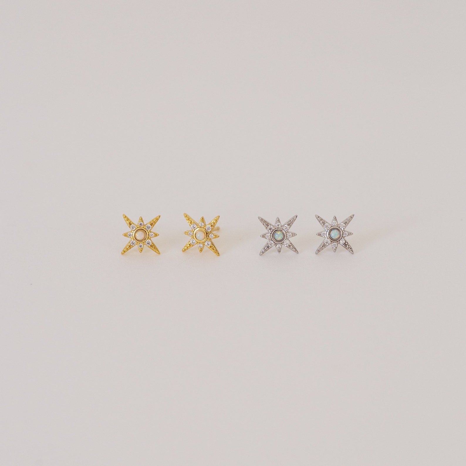 Two pairs of Starburst Studs—one gold, one silver—each adorned with a small central gem, reminiscent of diamond earrings, shown on a plain background.