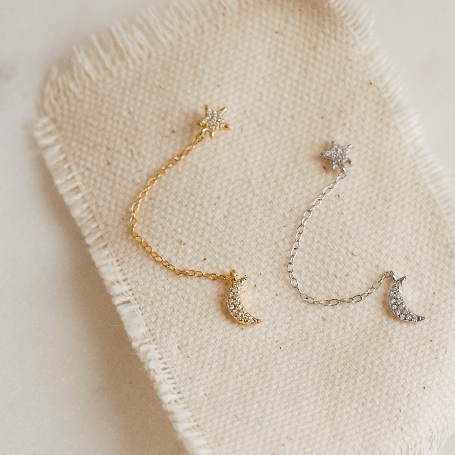 The Luna Moon & Star Chain Earrings, elegantly displayed on cloth, are perfect for adding a celestial touch to your cartilage piercing.