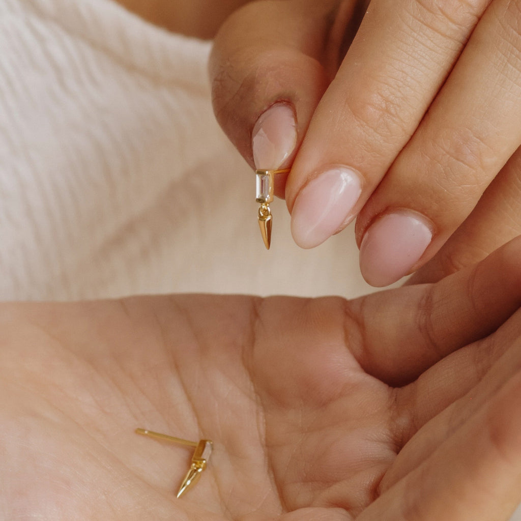 Close-up of hands holding a Wren Spike Stud earring with a pointed charm, while another stud rests on the palm, highlighting their lightweight design.
