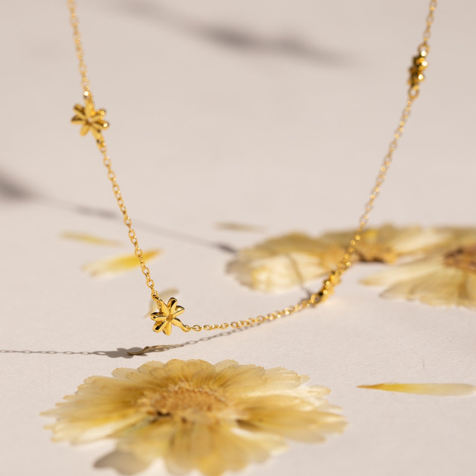 The Flower Child Necklace features small flower charms, perfect for layering. Shown above pressed yellow flowers, this boho piece adds a whimsical touch to any outfit.