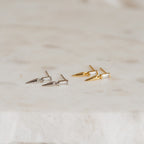 Two pairs of Wren Spike Studs, featuring spike-shaped designs in silver and gold with CZ baguette diamonds, rest elegantly on a marble surface.