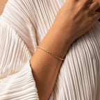 The Claudia Baguette Tennis Bracelet, featuring gold and sparkling baguette diamonds, adorns the wrist elegantly as it rests on white pleated fabric.