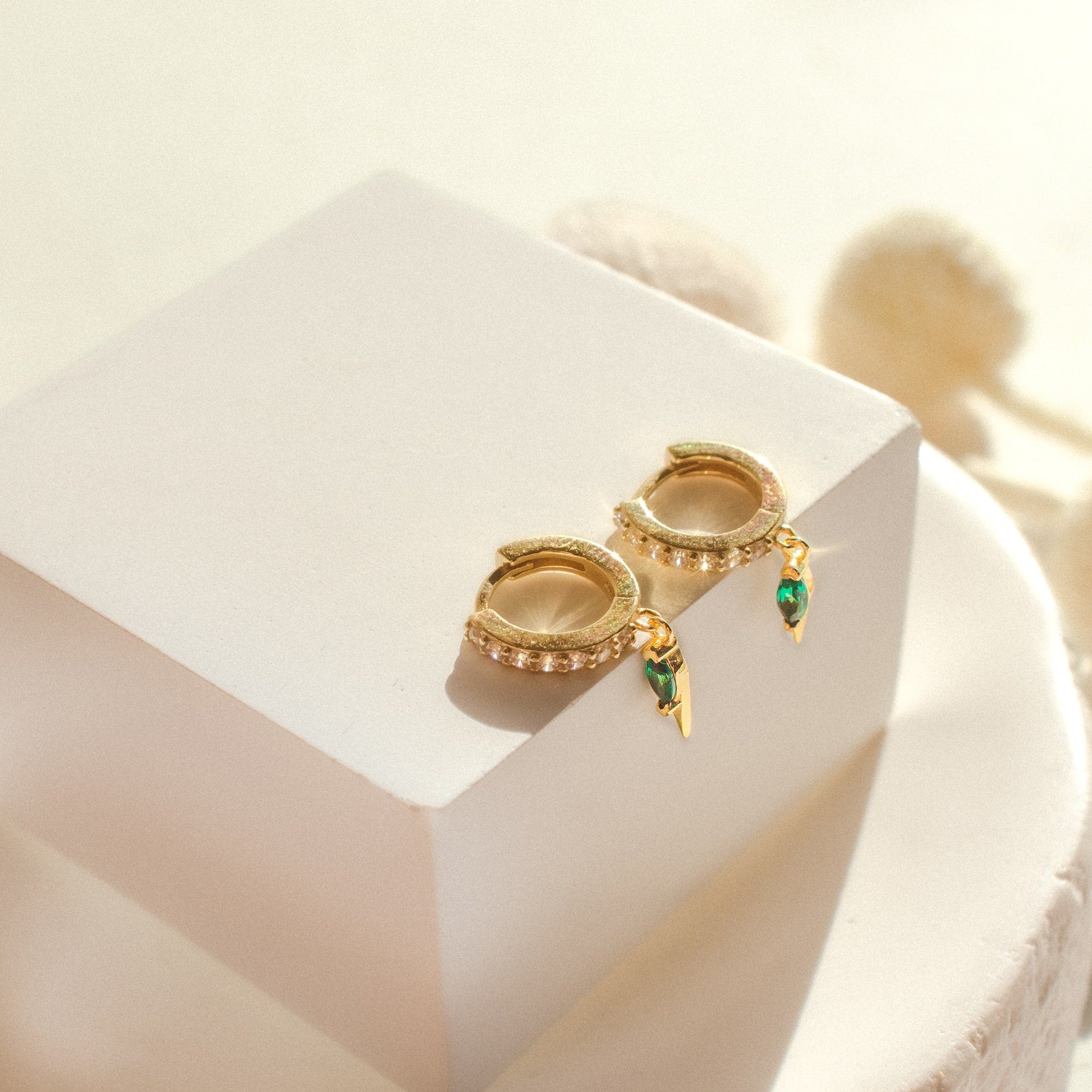 The Raine Emerald Dagger Huggies are displayed elegantly on a white cube—an ideal gift for her.