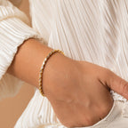 A person in a white pleated blouse wears the elegant Claudia Baguette Tennis Bracelet and has their hand in their pocket.