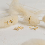 Odessa Marquise Studs, gold earrings featuring pearls and crystals, are shown on a white surface with beige dried flowers—an ideal delicate bridal gift.