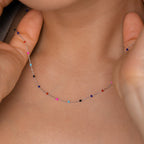 Close-up of a person wearing the Rainbow Station Necklace, a delicate silver piece adorned with small, colorful beads.