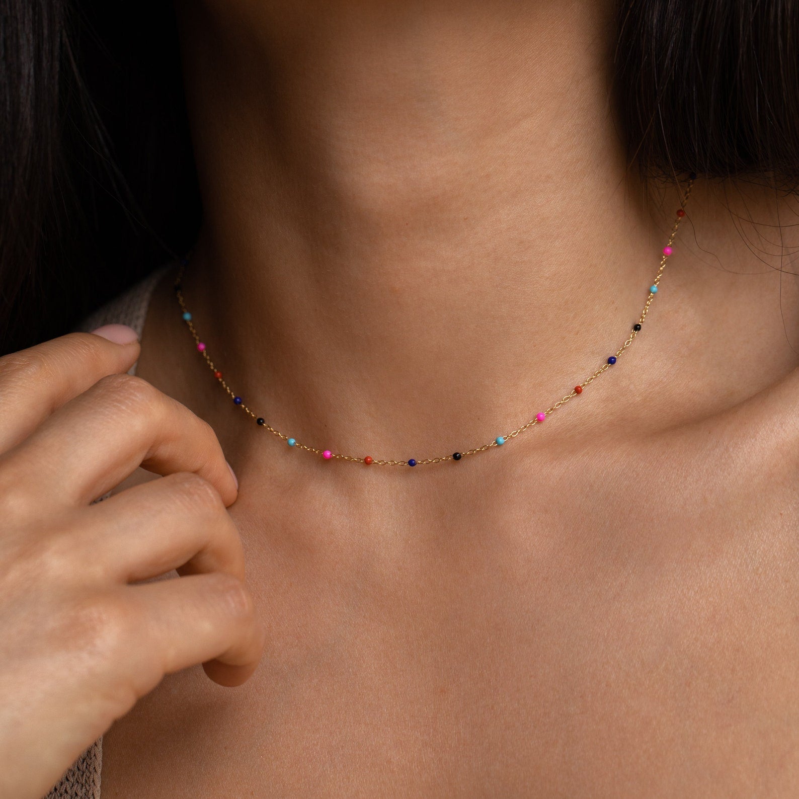 A close-up of a woman wearing the Rainbow Station Necklace, a delicate piece featuring small, colorful beads around her neck.