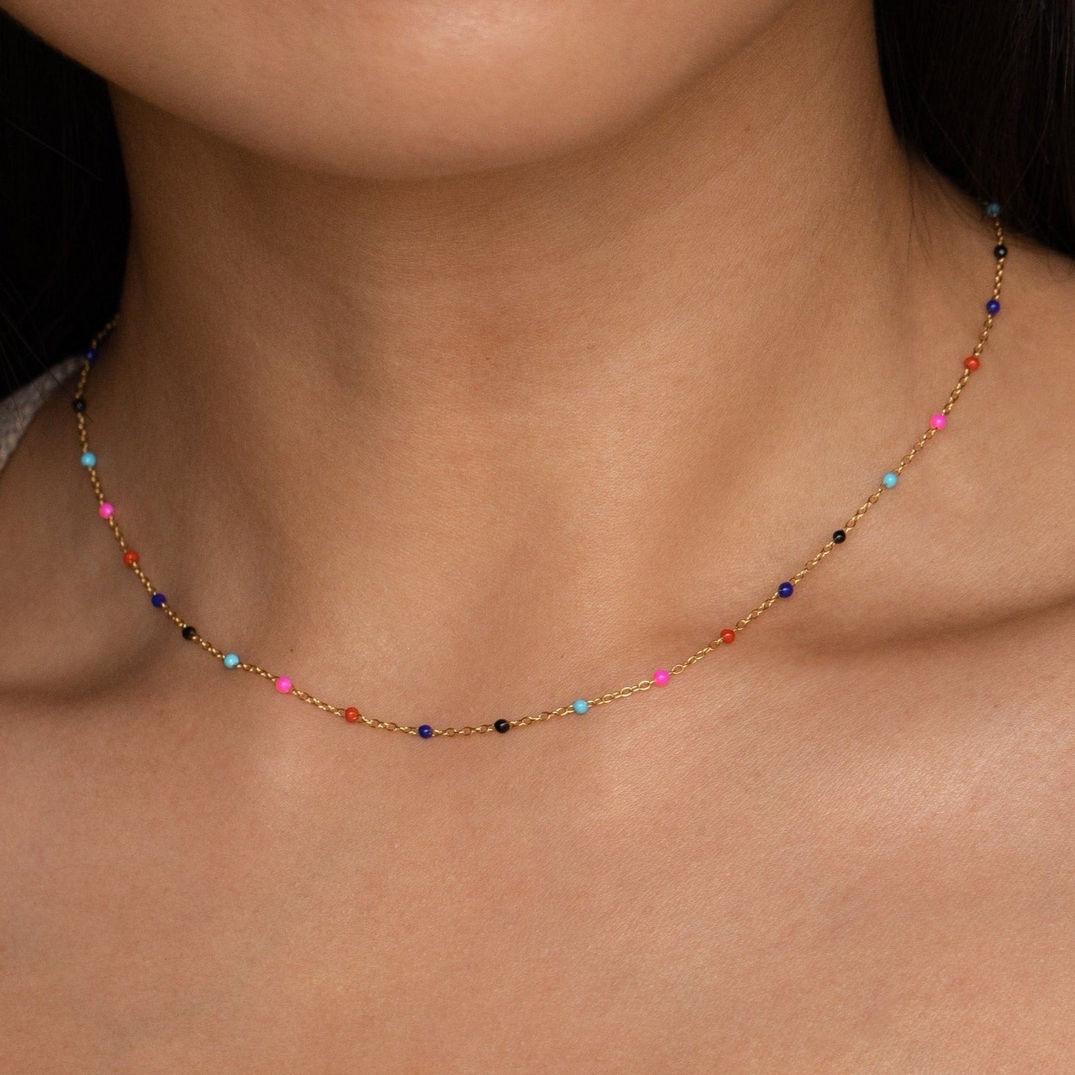 Close-up of a woman wearing the Rainbow Station Necklace, a delicate gold piece with small, colorful beads—perfect for adding a subtle touch to any look.