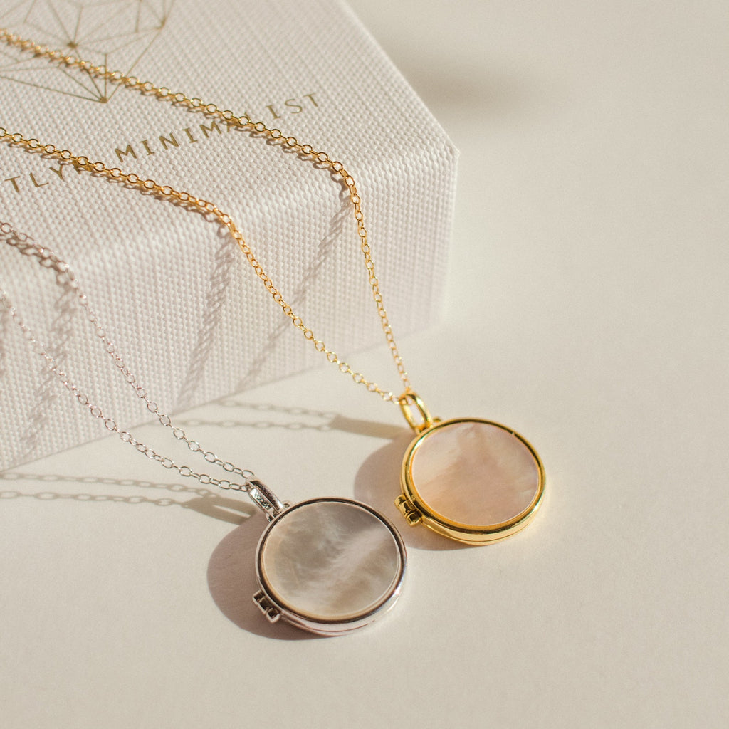 The Pearl Disc Locket Necklace, available in silver and gold, is displayed on chains next to a textured white box—making a meaningful gift.