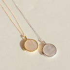Two round Pearl Disc Locket Necklaces—one gold, one silver—each with a light-colored stone center. This elegant set makes a meaningful gift and is beautifully displayed on a pale surface.