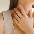 A woman with pale pink nails touches her neck, wearing the gold Traditional Initial Heart Signet Ring engraved with a monogram—an elegant piece that makes a perfect anniversary gift.
