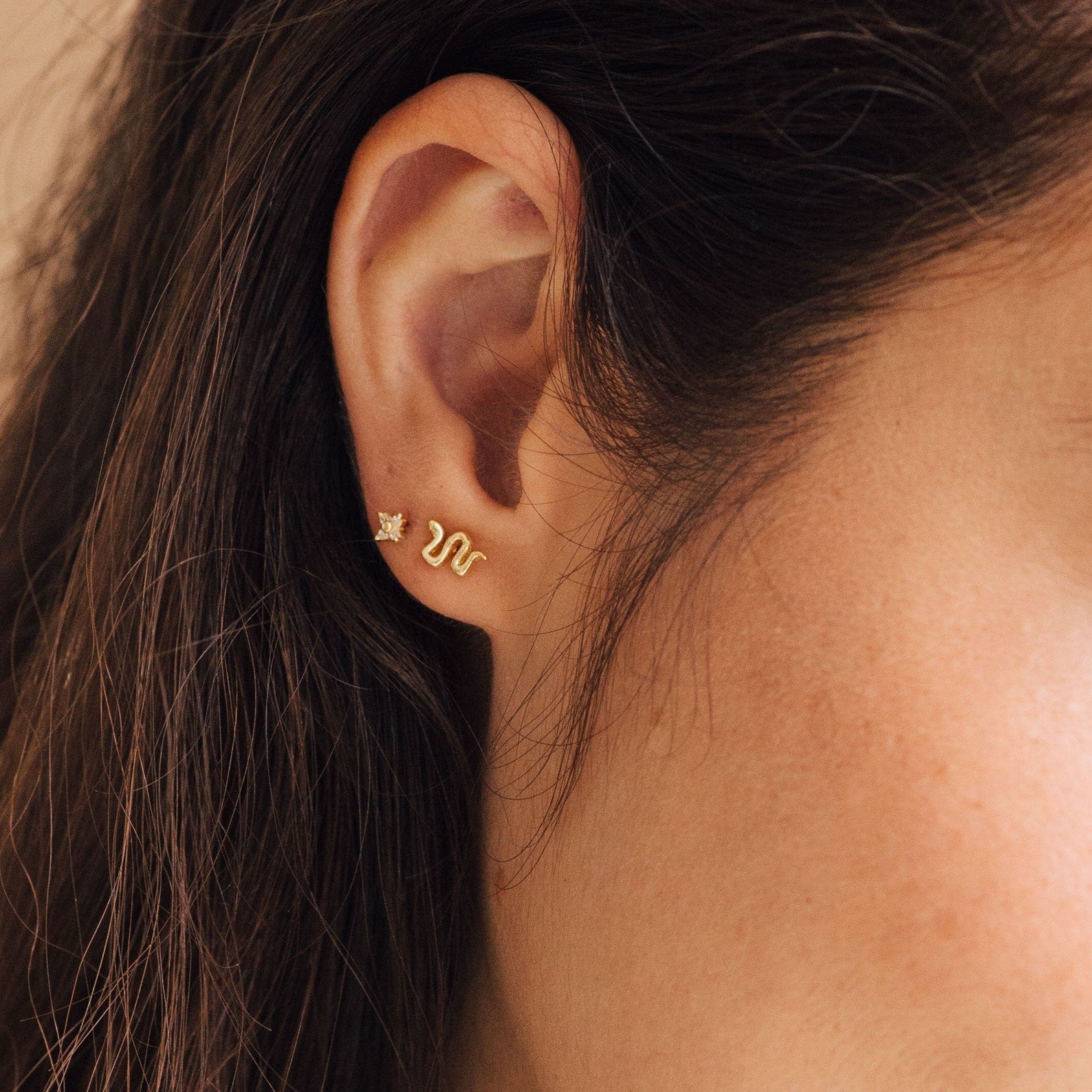 A close-up of a woman's ear wearing Tiny Python Studs for an elegant, dainty jewelry accent.
