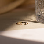 Celeste Duo Marquise Ring with two teardrop-shaped gemstones beside textured glass on a sunlit surface, highlighting its elegant open ring design.