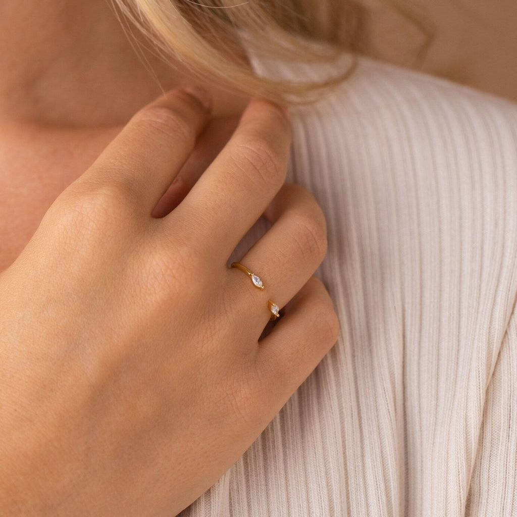 A hand wearing the gold Celeste Duo Marquise Ring with two small gemstones rests on pleated cream fabric.
